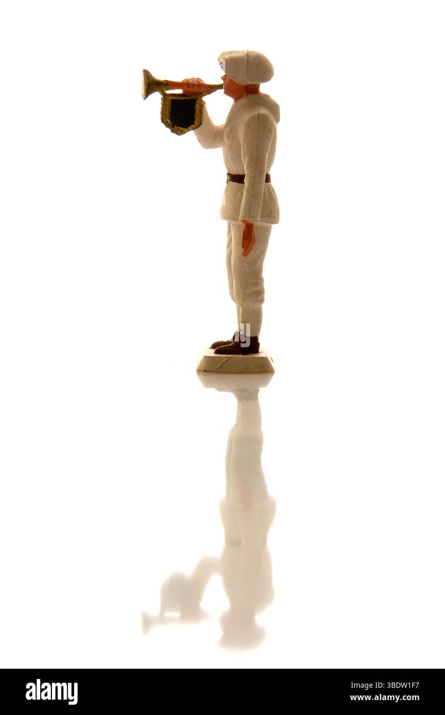 Una statuetta da soldato sta di profilo, indossa un'uniforme bianca e suona una tromba. Lo sfondo luminoso mette in risalto la silhouette del soldato. Foto Stock