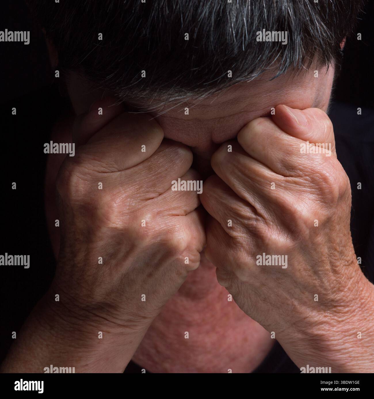 Una persona siede con la testa inchinata, le mani strette sugli occhi, trasmettendo emozioni e tumulti profondi. Foto Stock