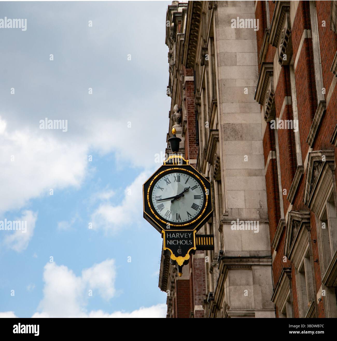 Orologio decorato di Harvey Nichols all'angolo di uno storico edificio in mattoni contro un cielo parzialmente nuvoloso Foto Stock