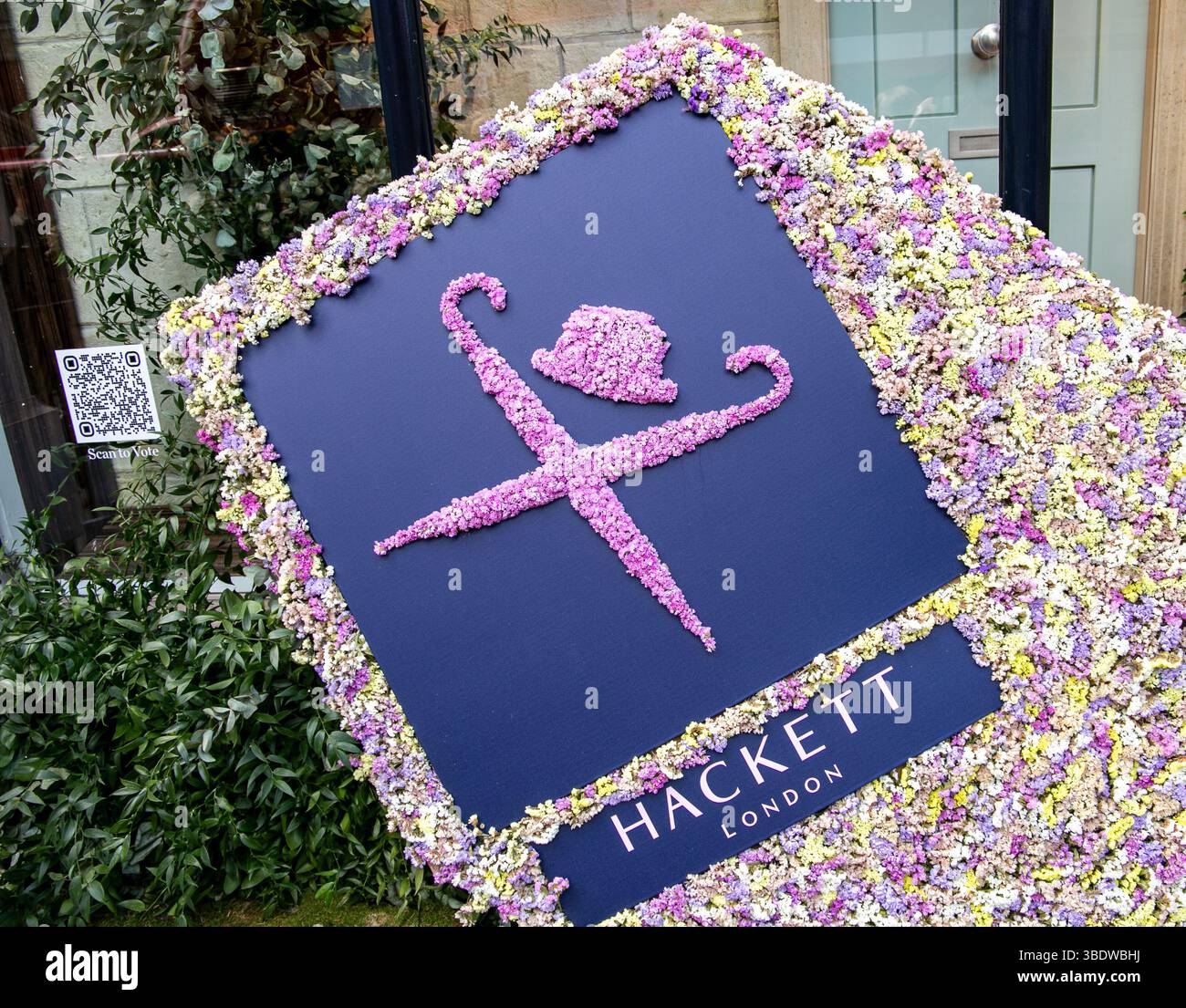 Grande esposizione floreale con il logo Hackett London realizzata con fiori vivaci all'esterno di un negozio all'entrata Chelsea in fiore 2025 Foto Stock