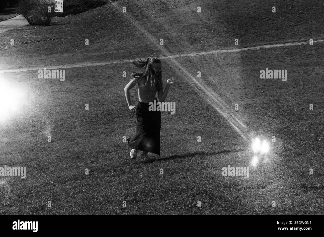 Donna che corre in salita attraverso un campo illuminato dal sole in bianco e nero Foto Stock