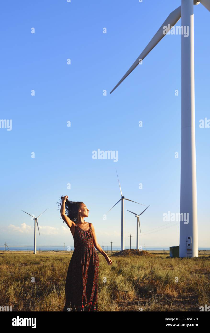 Donna elegante che balla nel campo con le turbine eoliche Foto Stock