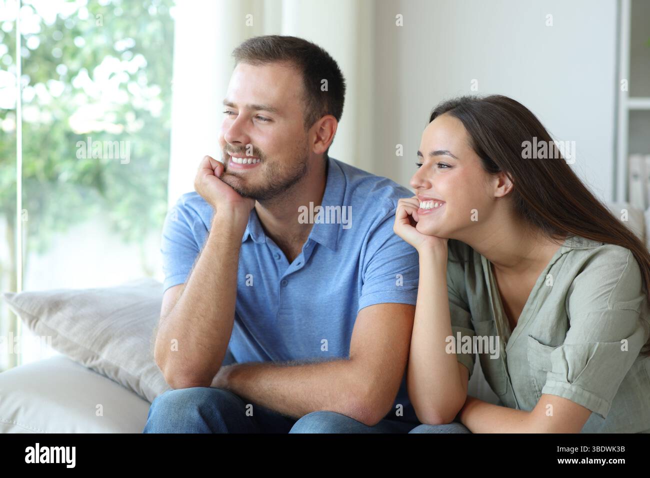 Coppia felice e rilassata che guarda attraverso una finestra seduta su un divano di casa Foto Stock