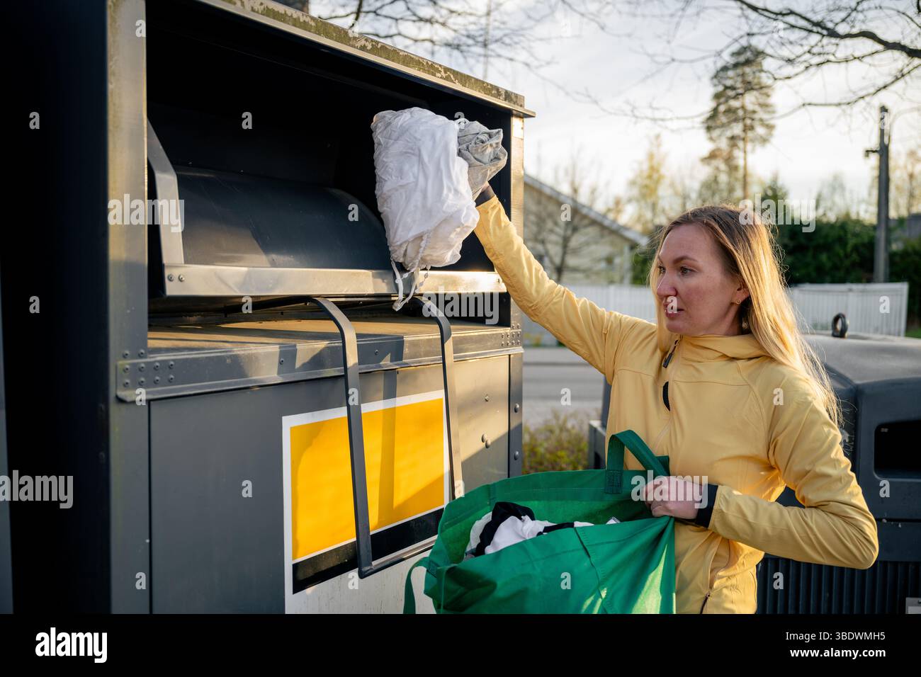 Donna che colloca vecchi vestiti usati nei contenitori per la raccolta differenziata Foto Stock