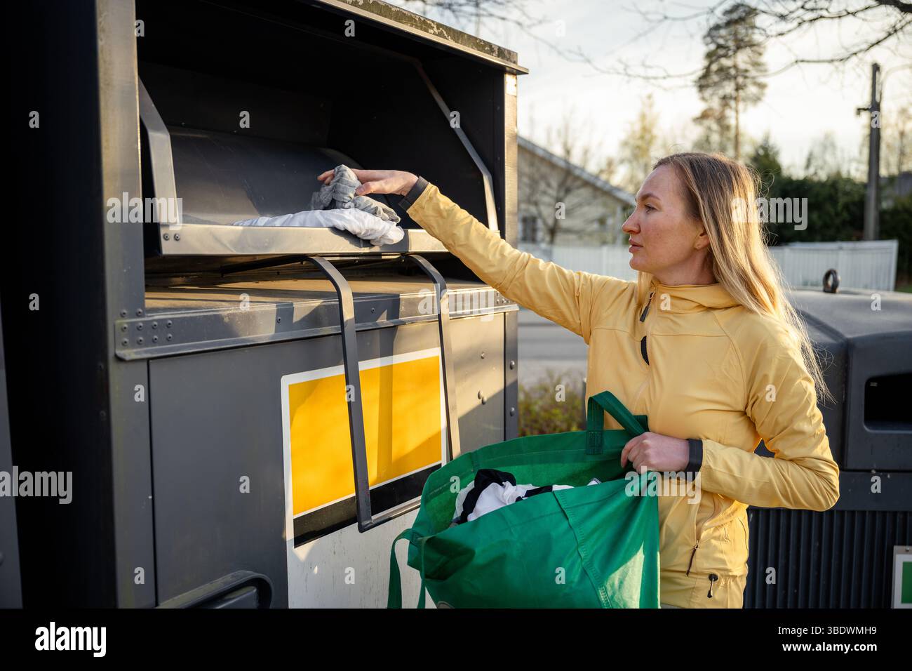 Donna che colloca vecchi vestiti usati nei contenitori per la raccolta differenziata Foto Stock