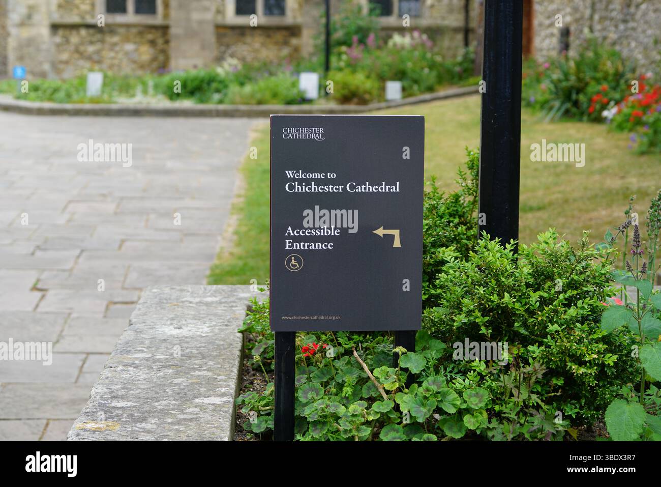 Cartello d'ingresso accessibile con sedia a rotelle alla Cattedrale di Chichester circondato da piante e sentieri. Chichester, Regno Unito Foto Stock
