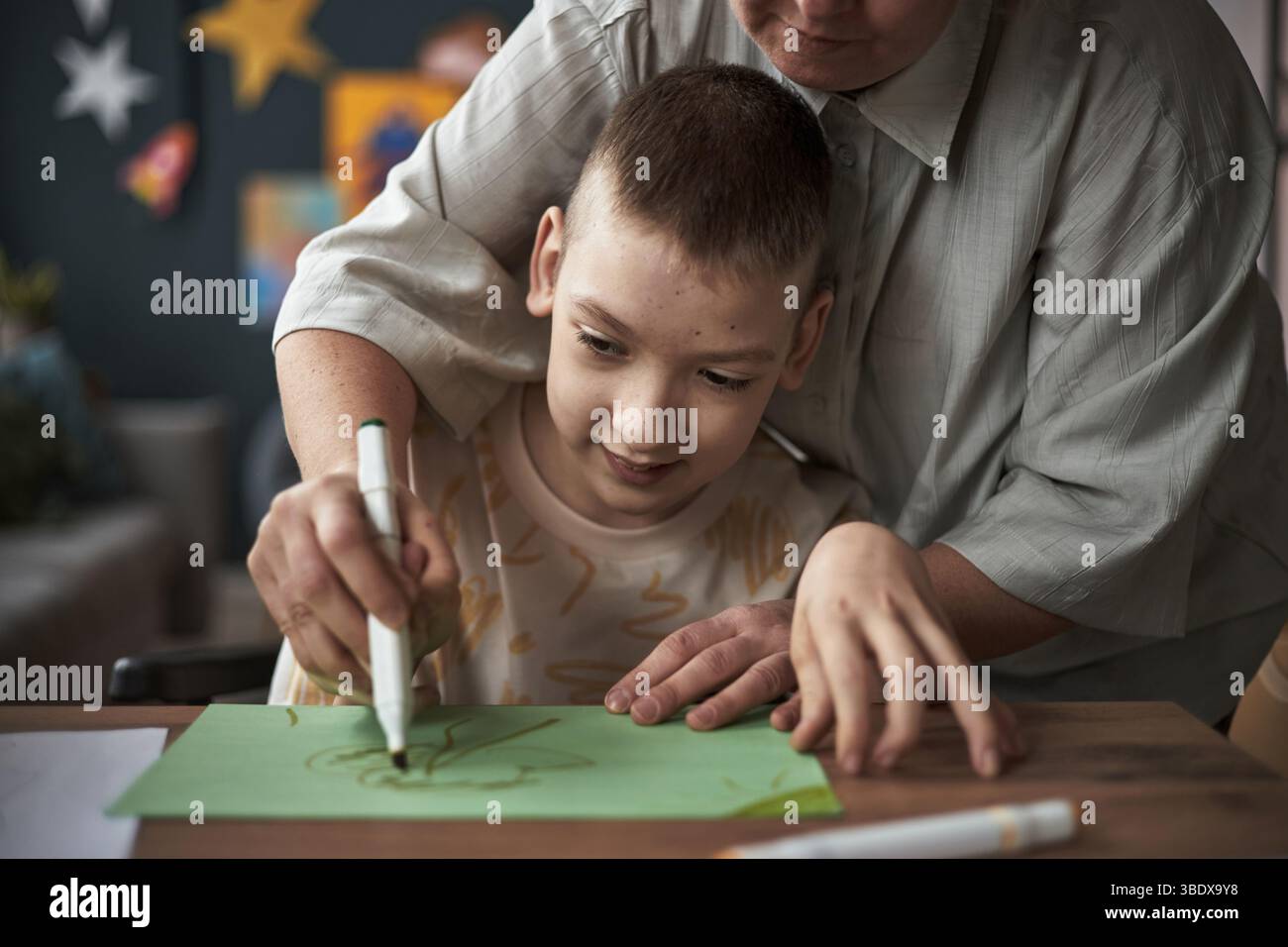 Ritratto di un bambino con disabilità che disegna forme intricate con le mani guida di un adulto avvolte dall'attenzione Foto Stock