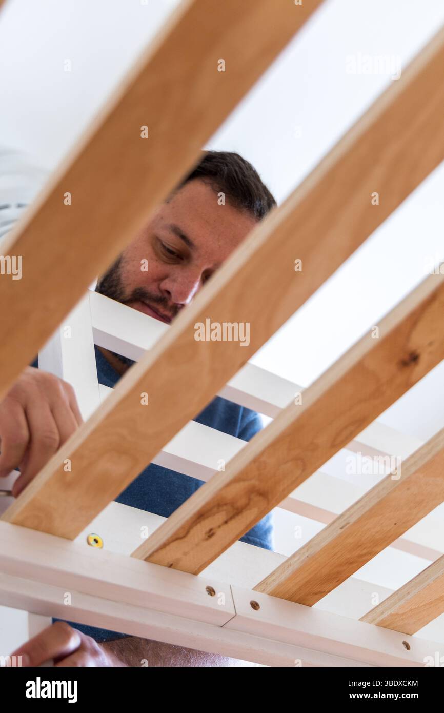 Un uomo sta lavorando su un telaio di legno. È concentrato sul compito che sta svolgendo ed è di umore serio Foto Stock Un uomo sta lavorando su un telaio di legno. È concentrato sul compito che sta svolgendo ed è di umore serio Foto Stock