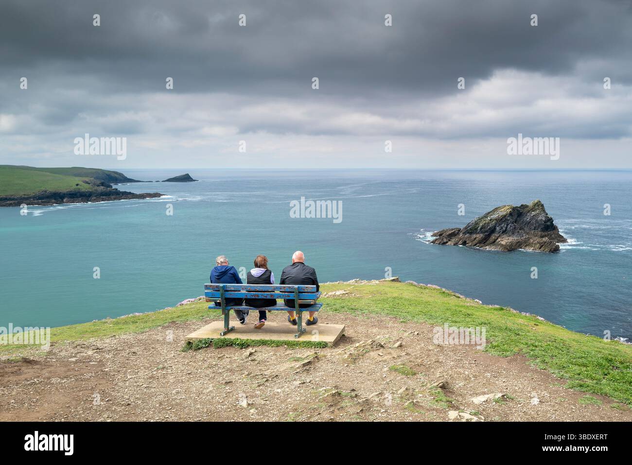 Tre turisti seduti su una panchina in cima a Pentire Point East che mostrano le piccole isole rocciose, Goose Rock e Chick on the c Foto Stock