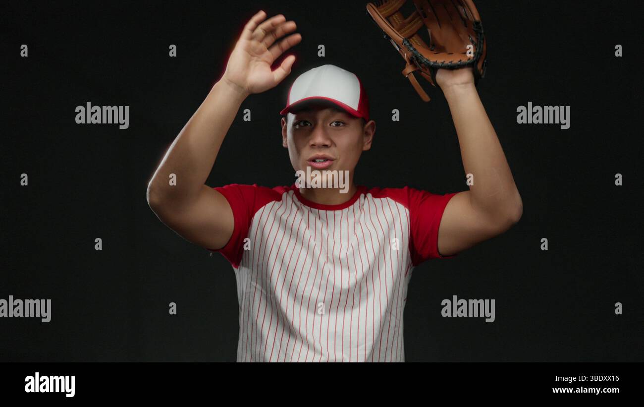 Il giovane cinese in uniforme da baseball posa con sicurezza con il guanto su sfondo nero isolato. Foto Stock