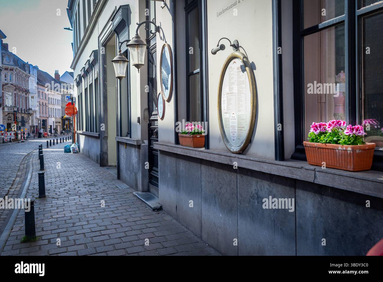 31.03.2025, Gent, Belgio, vista sul marciapiede, che mostra una facciata del ristorante con menu rotondi, lampade montate a parete, fiori rosa in vaso sulle finestre Foto Stock