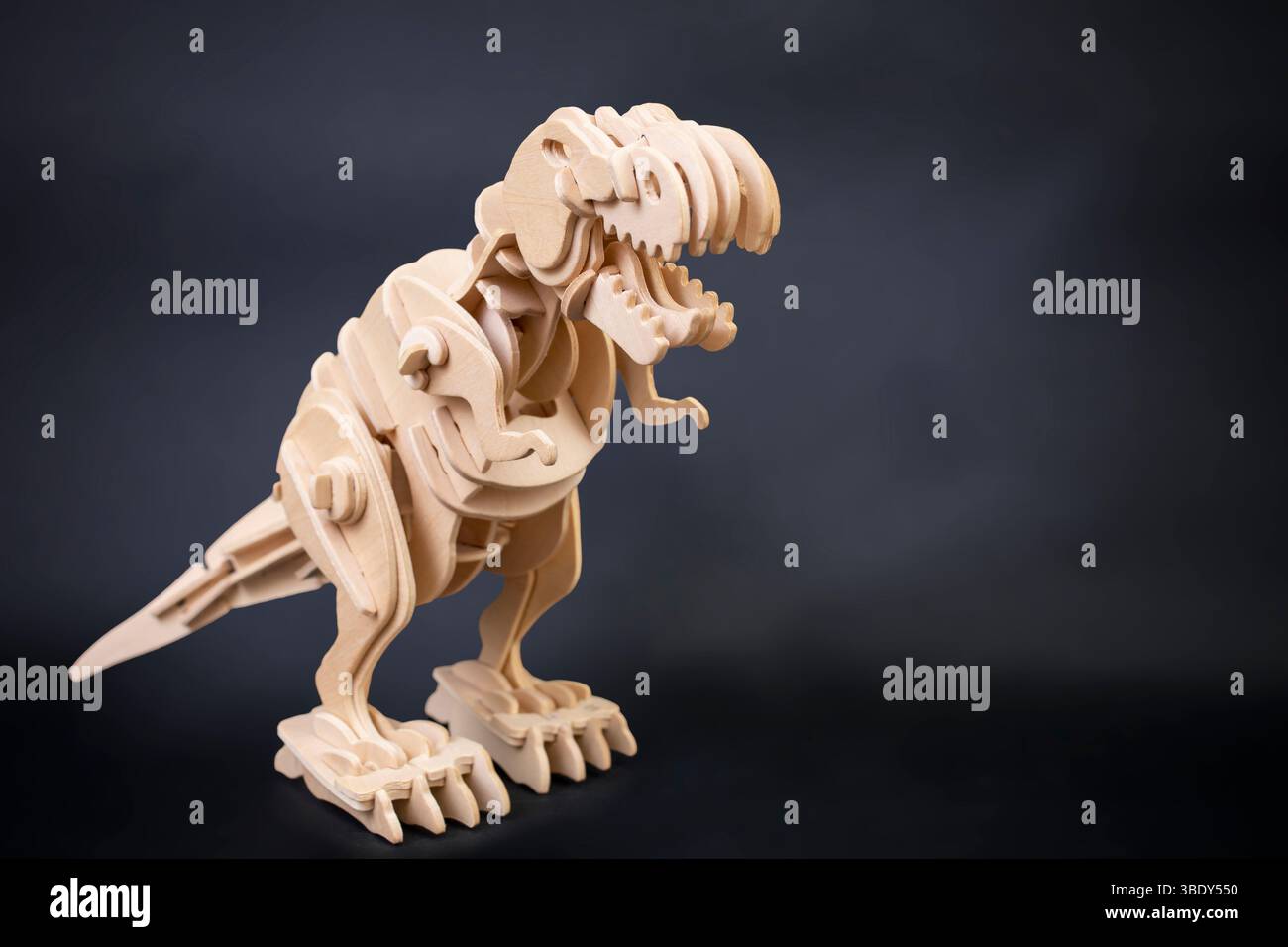 Puzzle in legno di dinosauro isolato su sfondo scuro, con spazio di copia Foto Stock