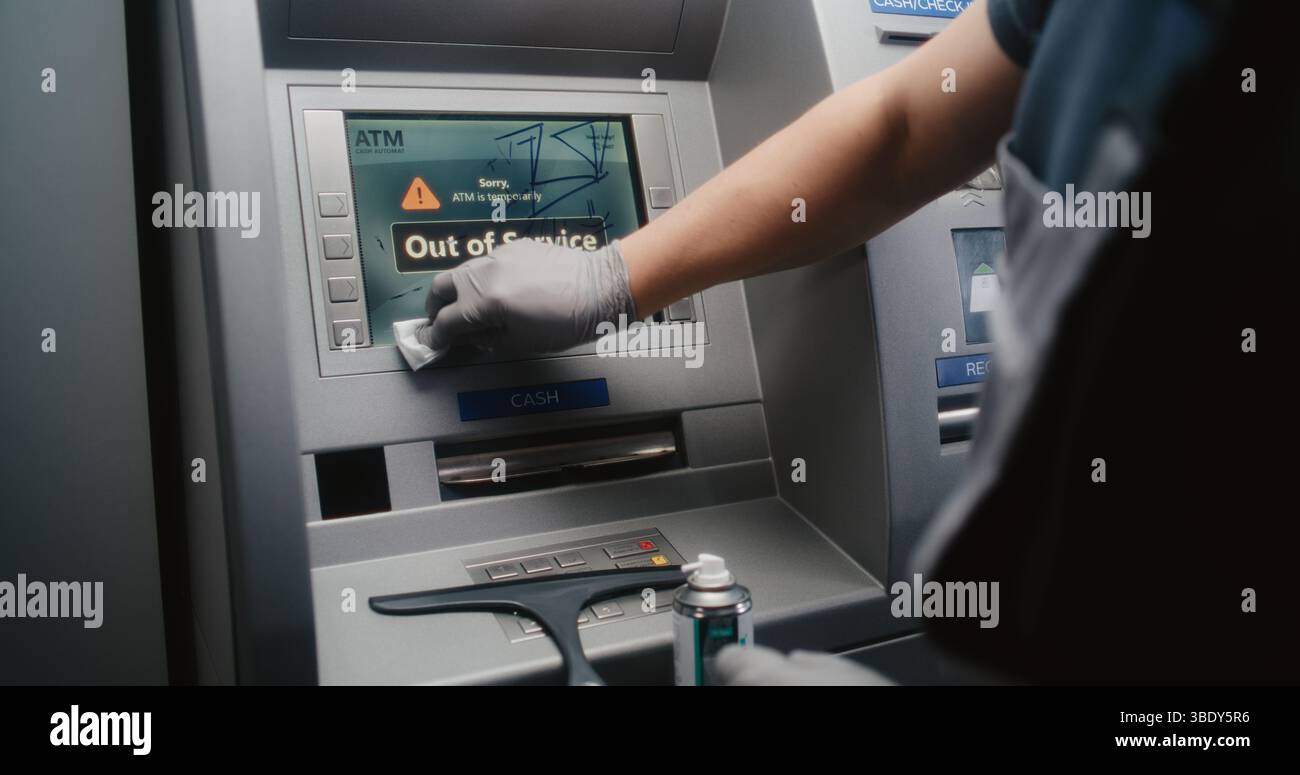 Pulizia pulizia dello schermo bancomat vandalizzato con Rag, rimozione di graffiti, etichette scarabocchiate da distributore automatico, bancomat. Servizio di pulizia, danni alla proprietà, atti vandalici delle apparecchiature bancarie pubbliche. Foto Stock