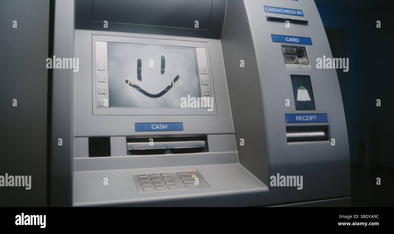 Vandalo irriconoscibile in vernice Graffiti spray con cappuccio su schermo ATM. Persona che danneggia illegalmente la proprietà, vandalizzando il bancomat fuori servizio. Criminalità urbana, vandalismo delle apparecchiature bancarie pubbliche. Foto Stock