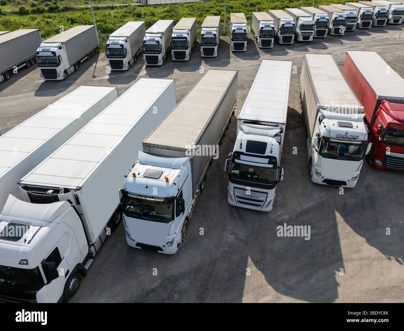 Vista aerea di un ampio parcheggio per camion in un hub logistico, con più semi-camion commerciali parcheggiati in file organizzate. Foto Stock