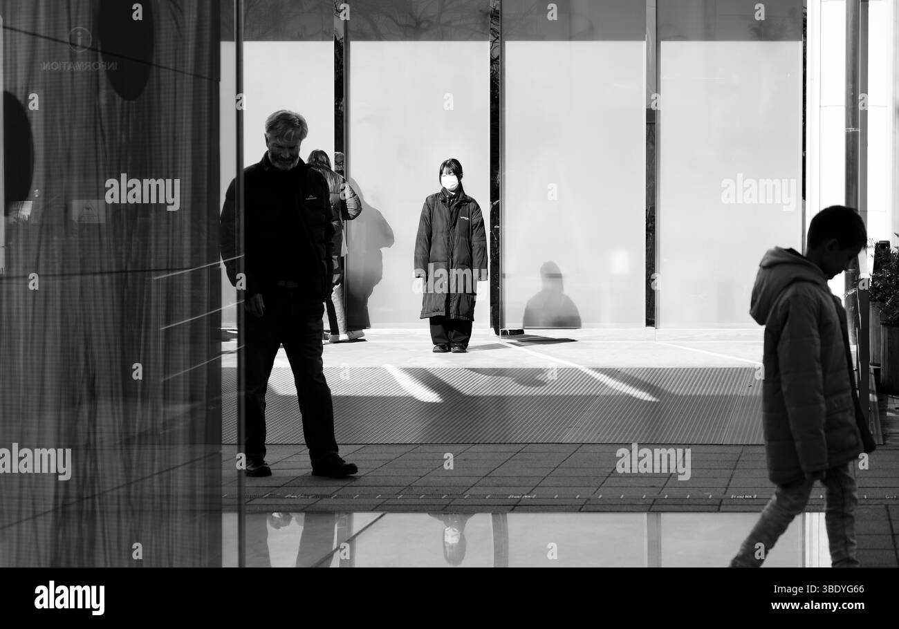 Il membro del personale mascherato si trova tranquillamente all'esterno dei pianeti TeamLab in bianco e nero Foto Stock