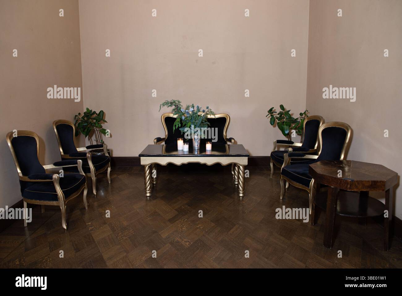 Un sofisticato salotto con poltrone vintage nero e oro, un tavolo centrale con candele e decorazioni floreali. Foto Stock