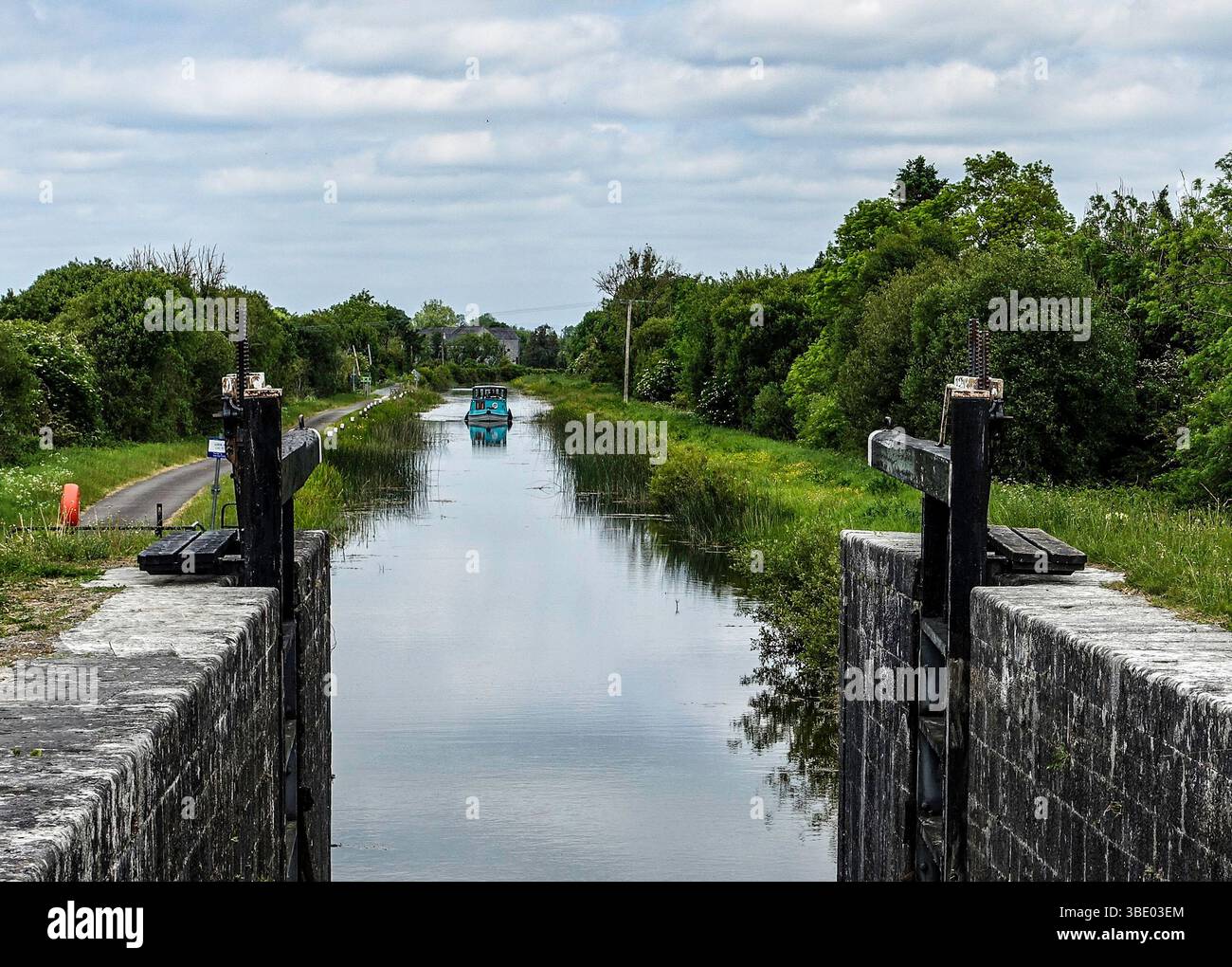 Vista da una chiusa in pietra sul Royal Canal, Cloondara, contea di Longford, Irlanda, con un motoscafo che si avvicina attraverso acque tranquille e alberate. Foto Stock