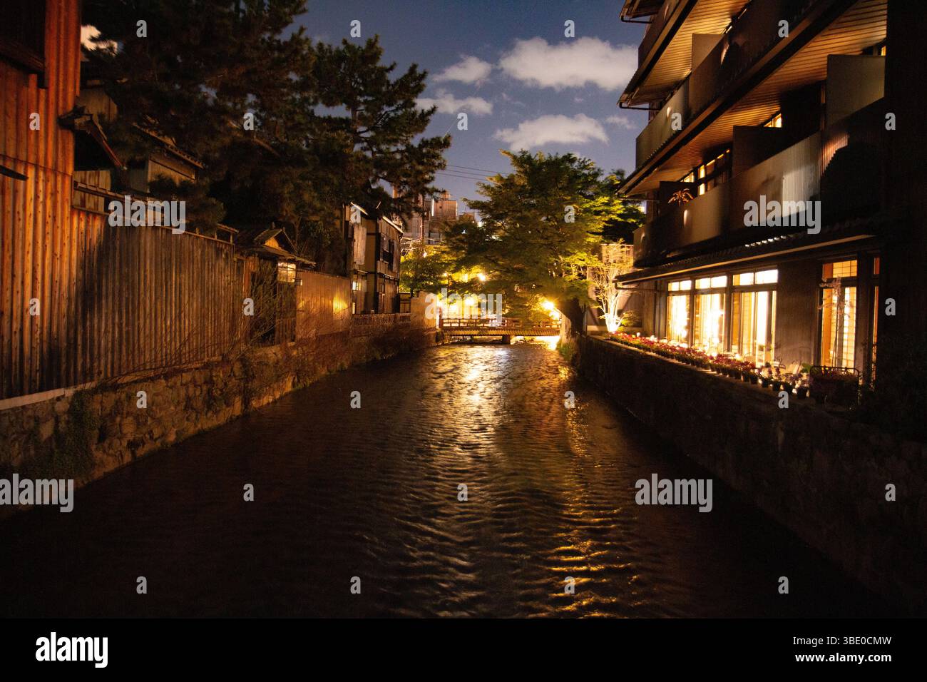 Canale di Kyoto illuminato di notte, fiancheggiato da case tradizionali e ciliegi, che riflettono la luce soffusa dell'acqua Foto Stock