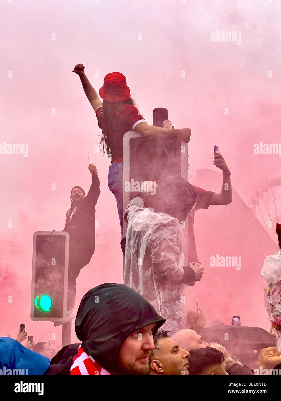 I tifosi festeggiano in cima ai semafori circondati dal fumo rosso durante la parata della vittoria del Liverpool sullo Strand, Liverpool, Regno Unito, 26 maggio 2025. Foto Stock