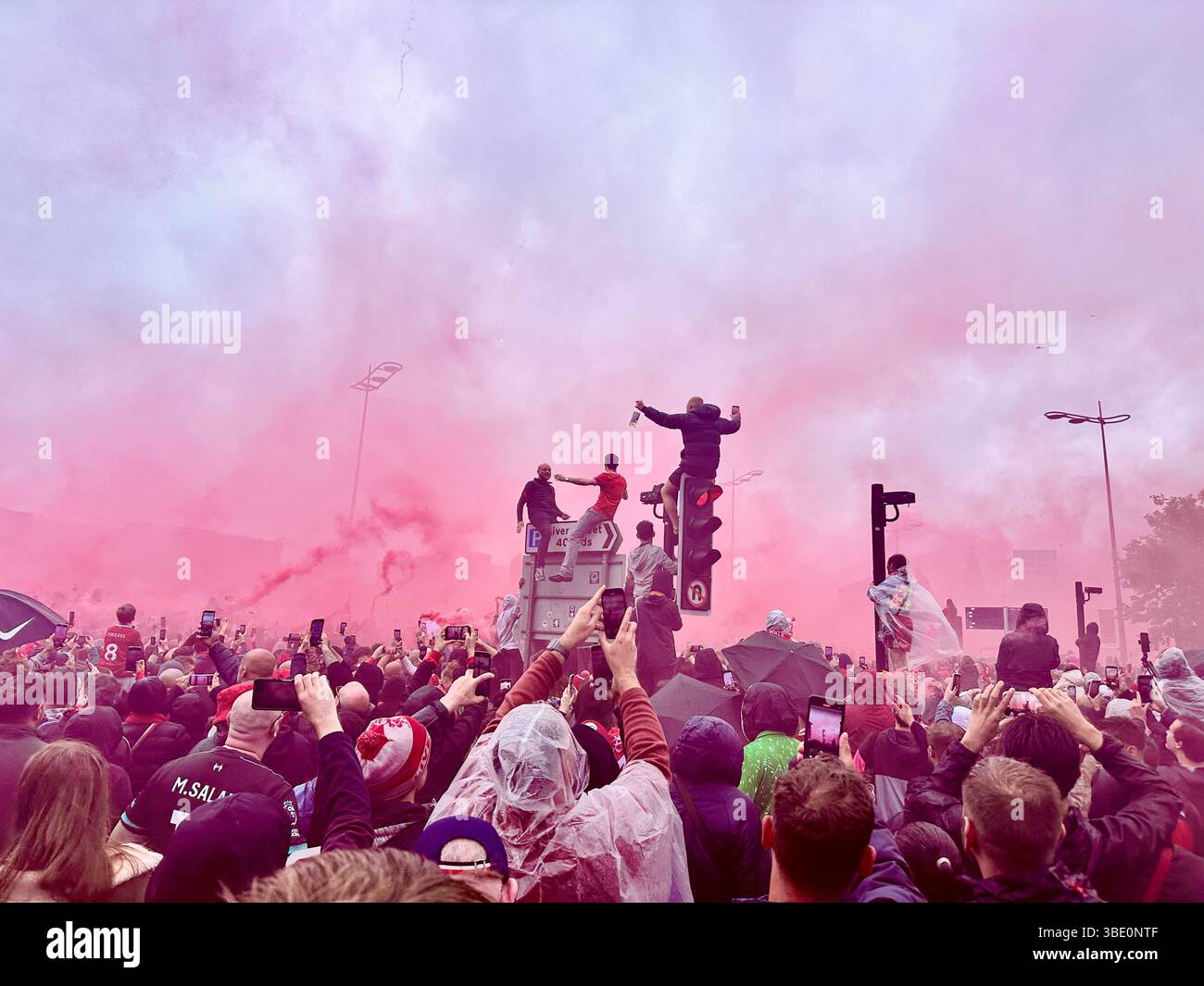 I tifosi del Liverpool ondeggiano rossi, si abbracciano e scalano i semafori durante la parata della vittoria di calcio su Strand Street, Liverpool, Regno Unito. 26 maggio 2025. - Immagine stock catturata con smartphone