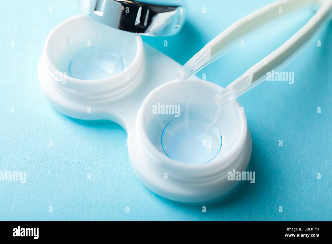 Lenti a contatto nella custodia e pinzette su sfondo azzurro, primo piano Foto Stock