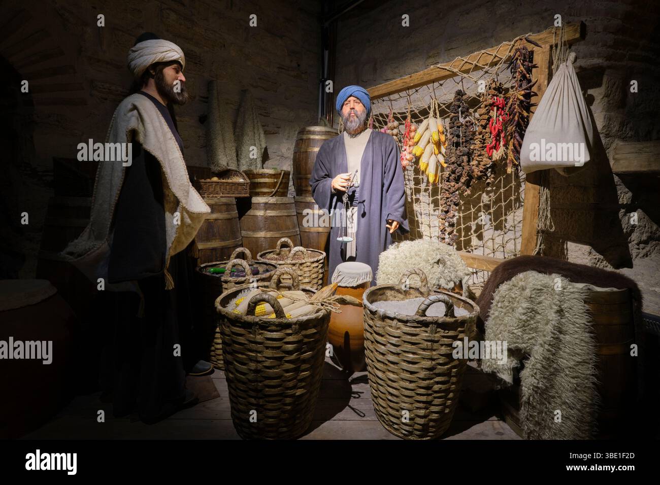 Un vecchio commerciante che usa una bilancia manuale per un compratore al suo banco in un mercato alimentare. Al Museo del Castello Kilibahir di Eceabat, Gallipoli, Turchia. Foto Stock