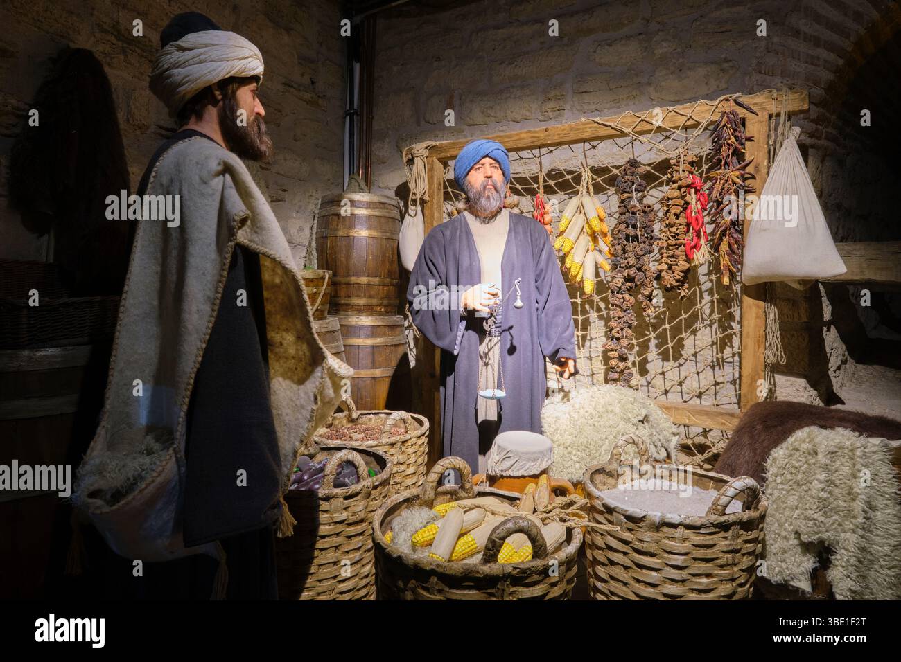 Un vecchio commerciante che usa una bilancia manuale per un compratore al suo banco in un mercato alimentare. Al Museo del Castello Kilibahir di Eceabat, Gallipoli, Turchia. Foto Stock