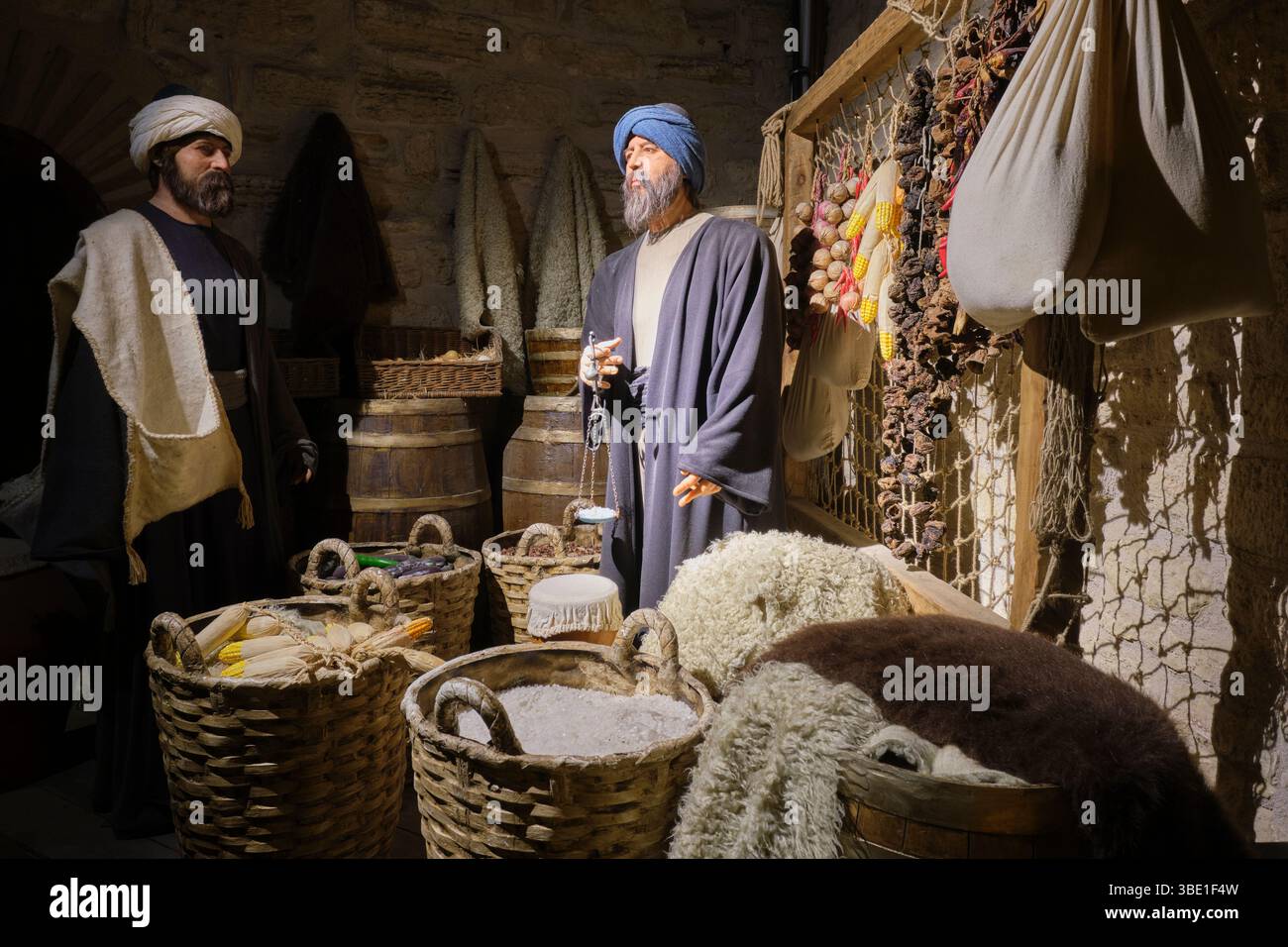 Un vecchio commerciante che usa una bilancia manuale per un compratore al suo banco in un mercato alimentare. Al Museo del Castello Kilibahir di Eceabat, Gallipoli, Turchia. Foto Stock