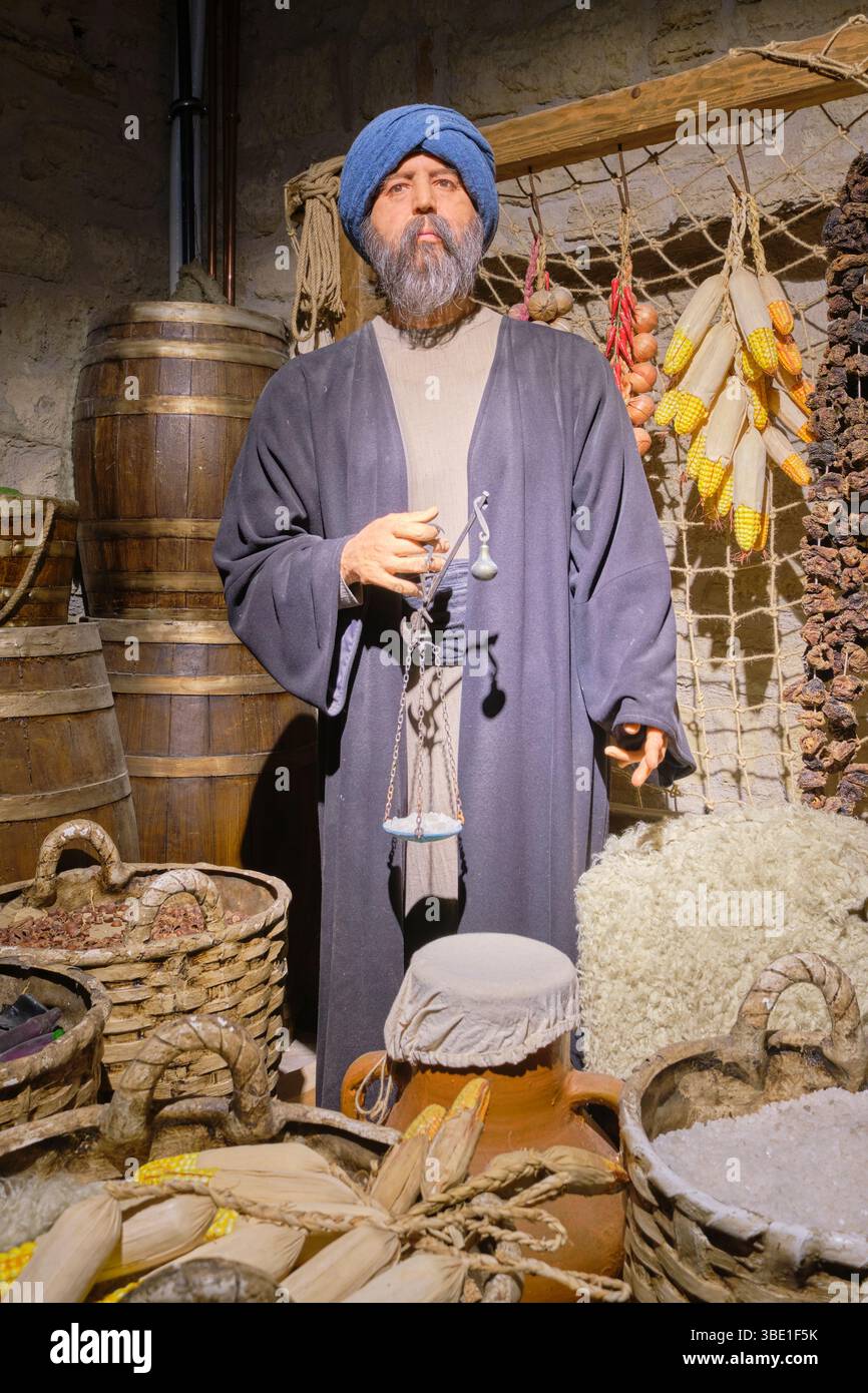 Un vecchio commerciante che usa una bilancia manuale per un compratore al suo banco in un mercato alimentare. Al Museo del Castello Kilibahir di Eceabat, Gallipoli, Turchia. Foto Stock