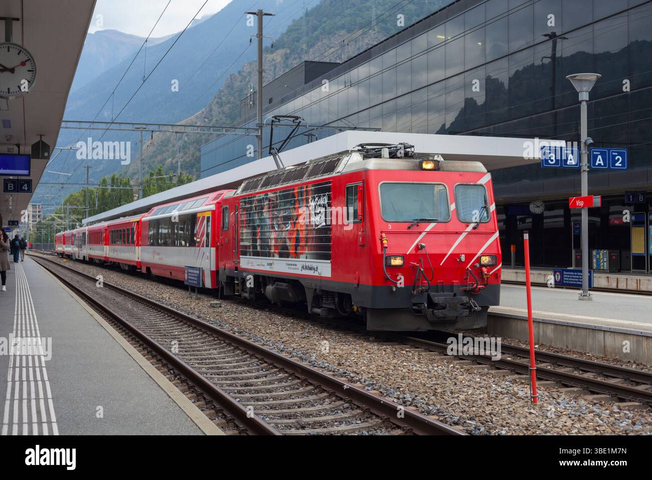 Matterhorn Gotthard Bahn HGe4/locomotiva elettrica a scartamento di 4 metri presso la stazione ferroviaria di Visp, Svizzera, con un treno passeggeri Foto Stock