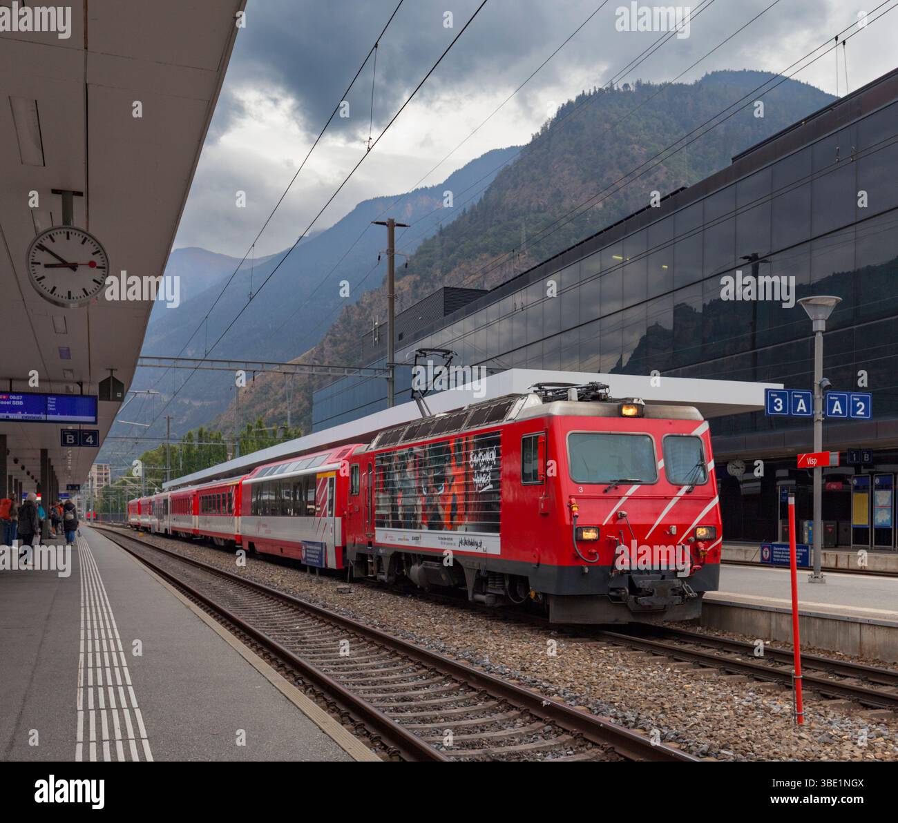 Matterhorn Gotthard Bahn HGe4/locomotiva elettrica a scartamento di 4 metri presso la stazione ferroviaria di Visp, Svizzera, con un treno passeggeri Foto Stock
