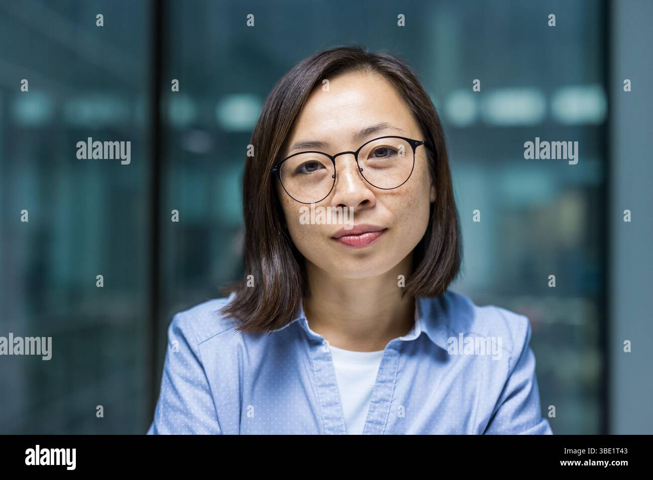 Una donna asiatica pronta con occhiali e un'espressione premurosa posa per un ritratto, ben illuminata e focalizzata. Foto Stock