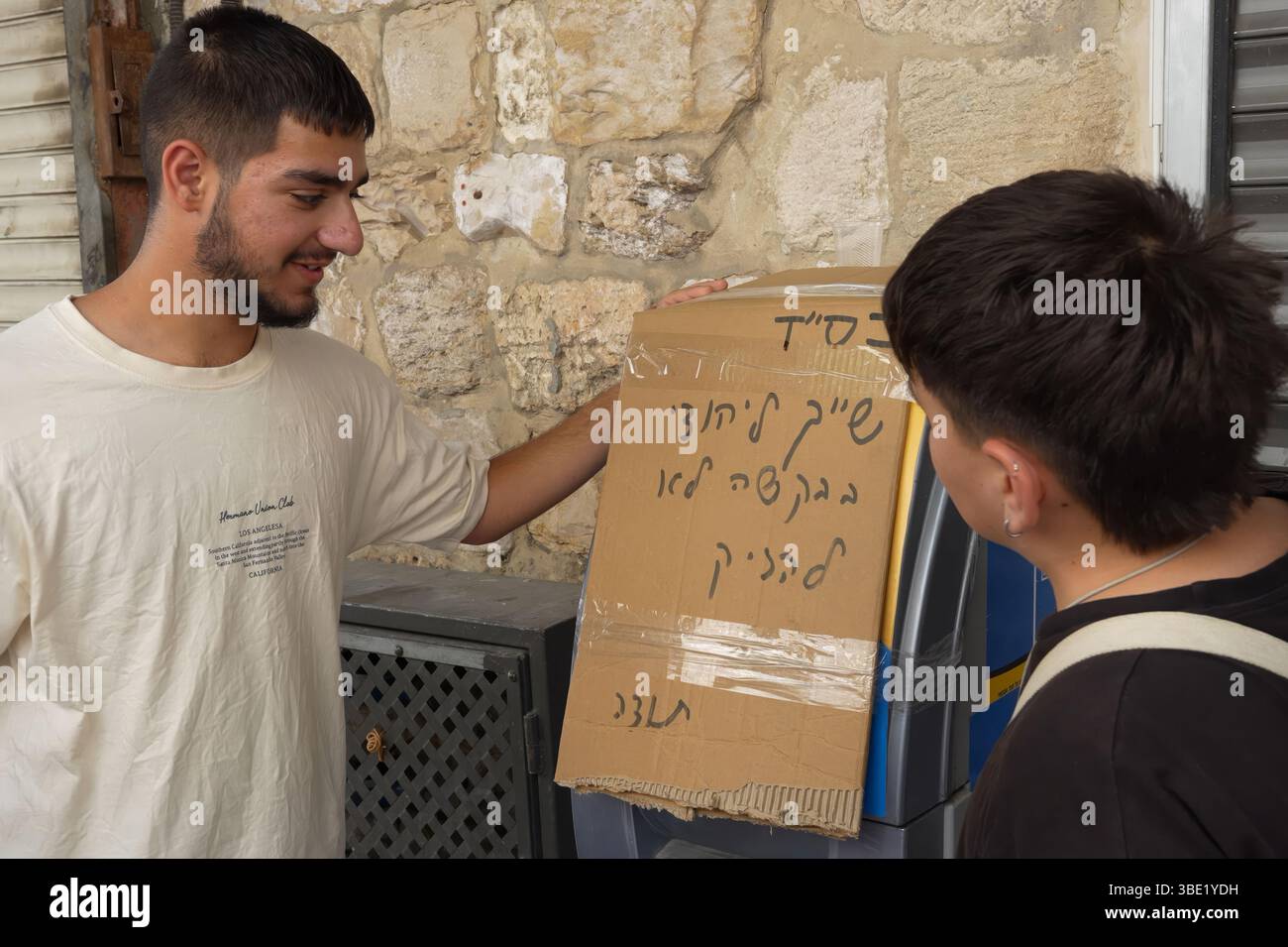GERUSALEMME - MAGGIO 26: I giovani israeliani ultra-nazionalisti guardano ad una macchina ATM con un segno che dice "questo appartiene agli ebrei. Per favore, non danneggiare." Mentre marciano attraverso la via al-Wad nel quartiere musulmano durante la "marcia della bandiera" nazionalista ebrea per celebrare il "giorno di Gerusalemme" nella città Vecchia il 26 maggio 2025 a Gerusalemme. La controversa marcia annuale degli israeliani nazionalisti vede migliaia di persone sfilare attraverso la città Vecchia di Gerusalemme per segnare la cattura dell'ex-giordana ad est della città durante la guerra dei sei giorni nel 1967. Foto Stock