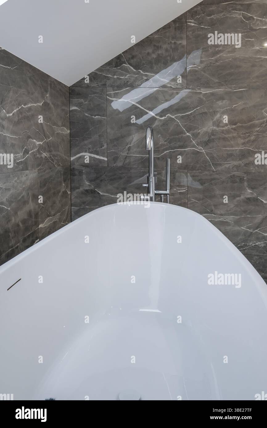 Bagno contemporaneo con lavandino bianco su ripiano in legno, doccia in vetro con gocce di pioggia e pareti piastrellate grigie. Foto Stock
