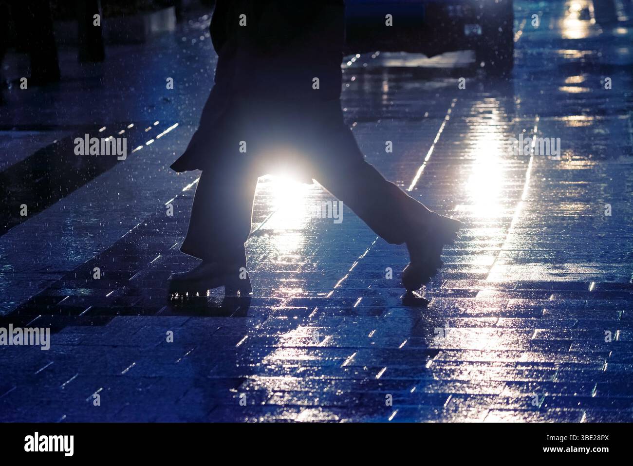 Piedi di persona che attraversano la strada acciottolata contro l'auto di notte Foto Stock
