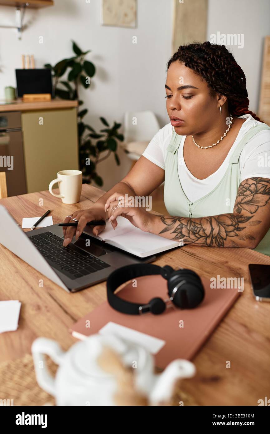 Una giovane donna afroamericana lavora diligentemente sul suo laptop in un ambiente domestico luminoso. Foto Stock