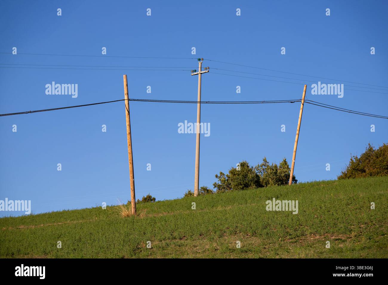 Le linee elettriche rurali attraversano verdi colline sotto un cielo azzurro. Foto Stock