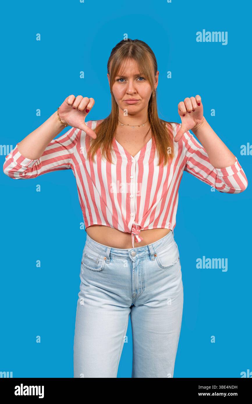 Giovane donna che mostra un gesto verso il basso che esprime disprezzo e disapprovazione su sfondo blu Foto Stock