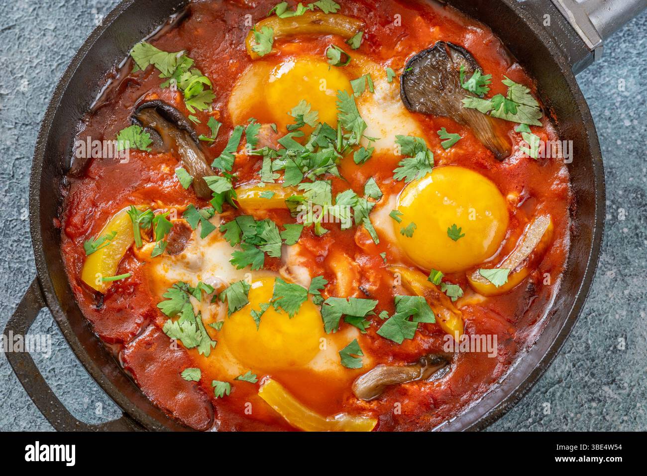 Uova sospese a base di pomodoro speziato con funghi, peperoni ed erbe fresche Foto Stock