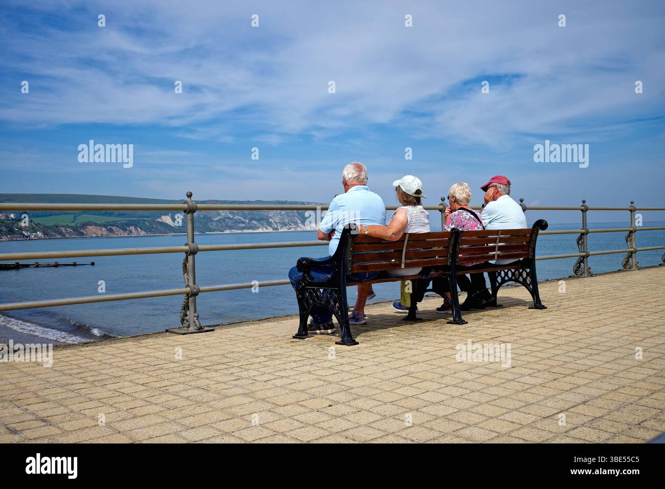 Vista posteriore di due coppie anziane sedute su una panchina che si affaccia su Swanage Bay in un giorno d'estate, Dorset Inghilterra, Regno Unito Foto Stock