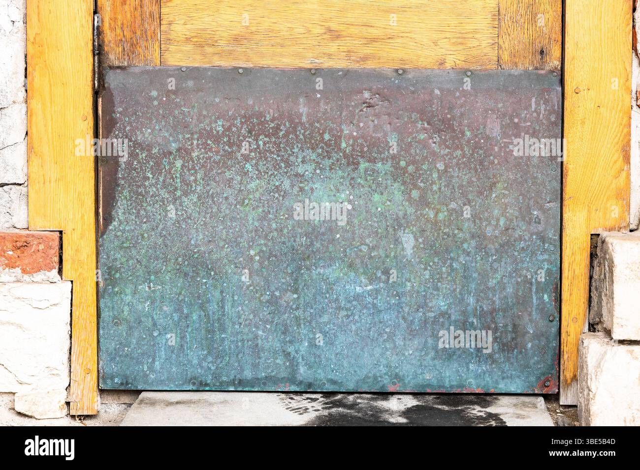 la superficie verde e rossa marrone della vecchia piastra di rame chiude il foro della porta esterna Foto Stock
