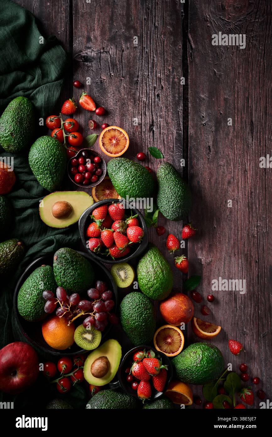 Un vivace assortimento di frutta e verdura fresca, tra cui avocado, fragole, uva e agrumi, disposto ad arte su un rustico legno scuro Foto Stock