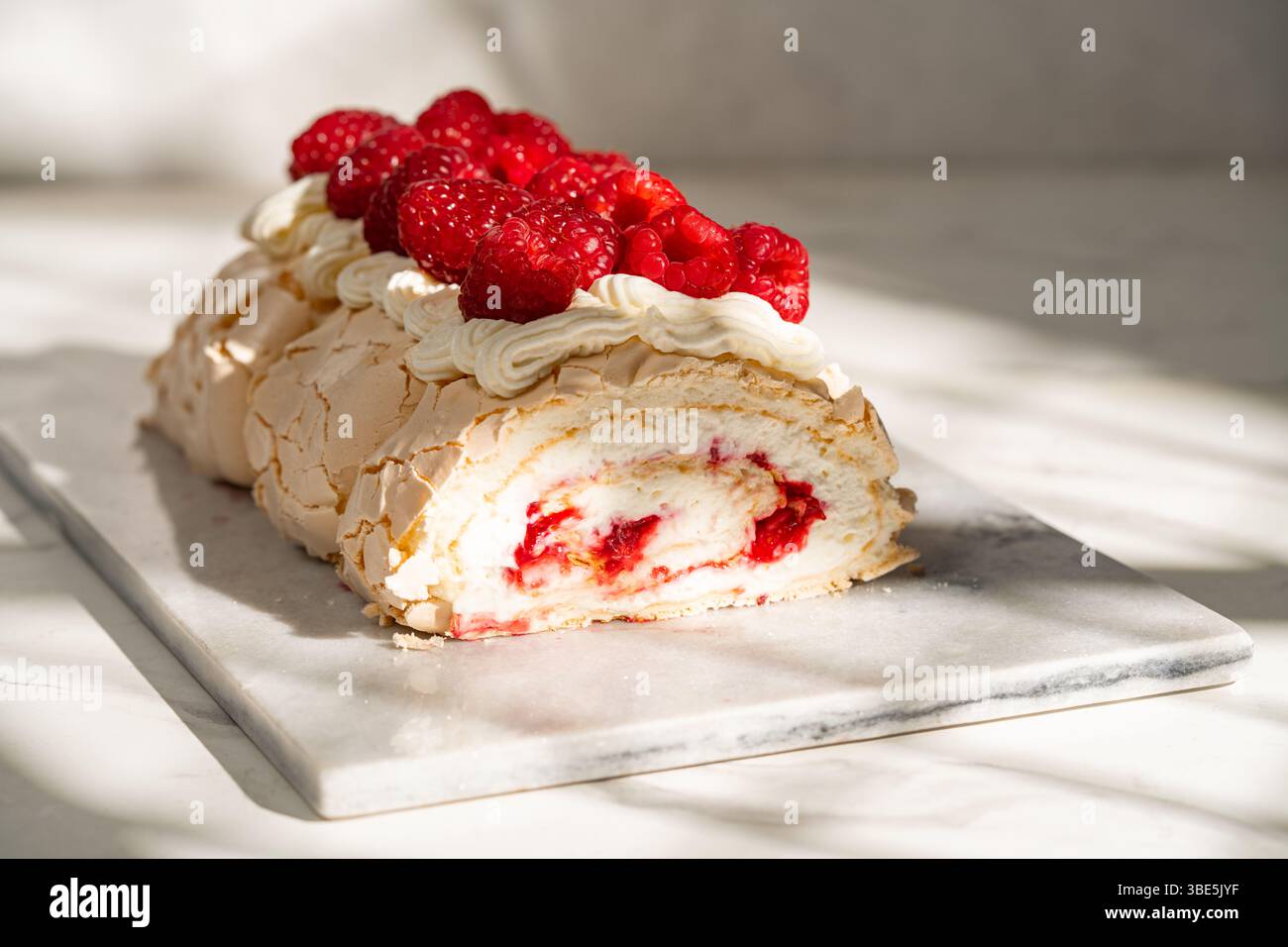 Una deliziosa roulata di meringa di lamponi ripiena di panna ricca e condita con lamponi freschi. Il dessert perfetto per una combinazione di dolci e crostate Foto Stock