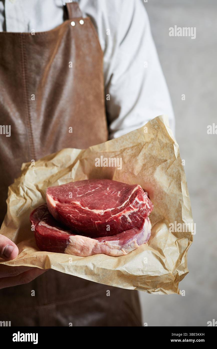 Un macellaio esperto contiene carne appena tagliata avvolta in carta marrone. L'attenzione è rivolta alla consistenza marmorizzata della carne, che mette in mostra qualità e artigianalità Foto Stock