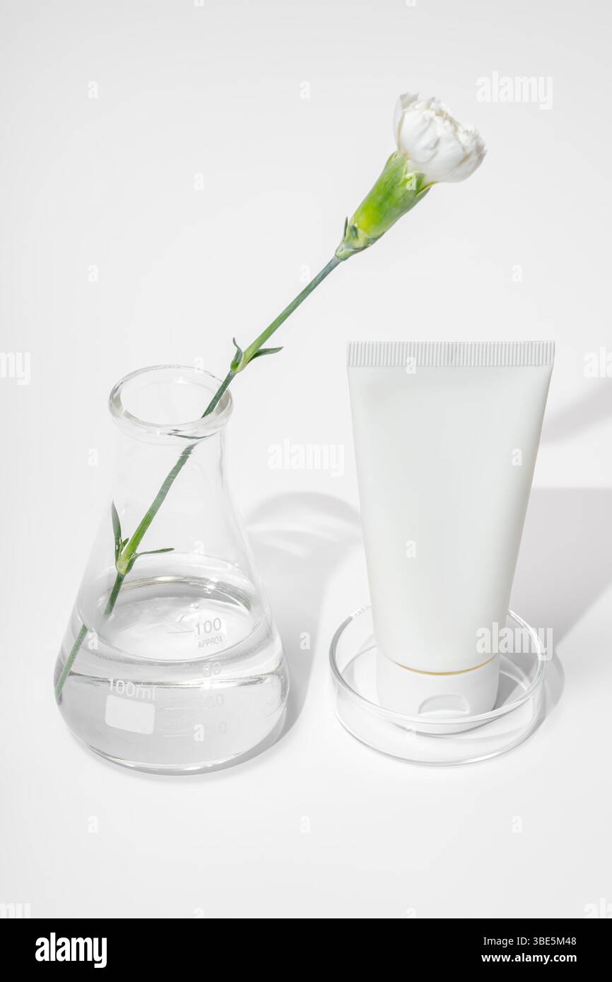 Un moderno laboratorio per la cura della pelle con un gambo di fiori bianco che si estende attraverso una fiasca trasparente e un tubo bianco di crema, che simboleggia il biologico e la sciente Foto Stock