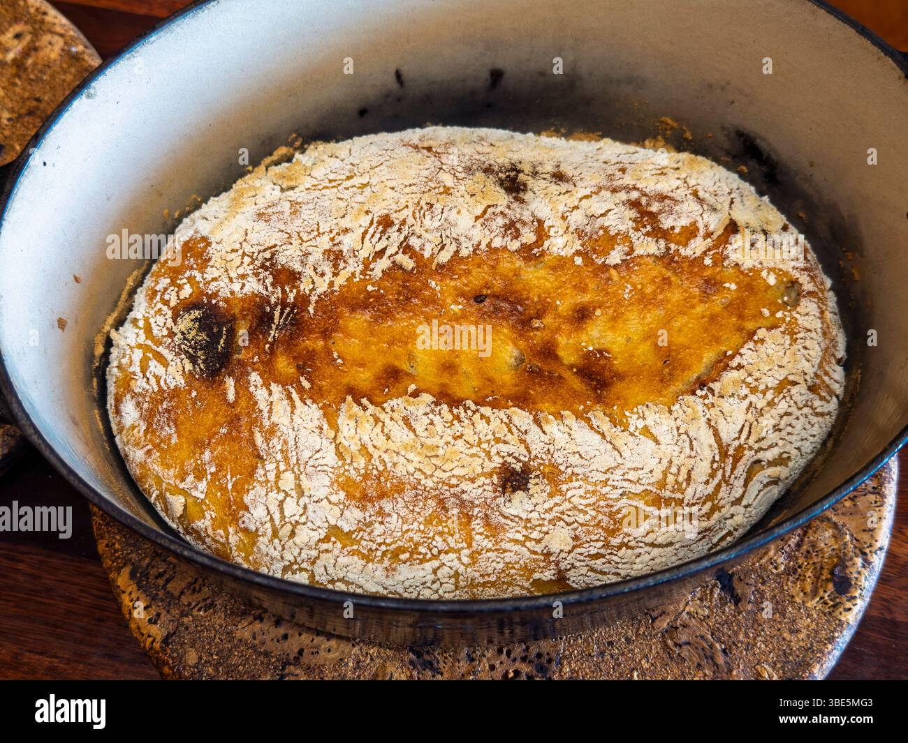 Il pane rustico appena sfornato riposa in una pentola di ghisa, con una crosta dorata. Lo sfondo in legno aggiunge calore e un'atmosfera casalinga a questo appetitoso Foto Stock