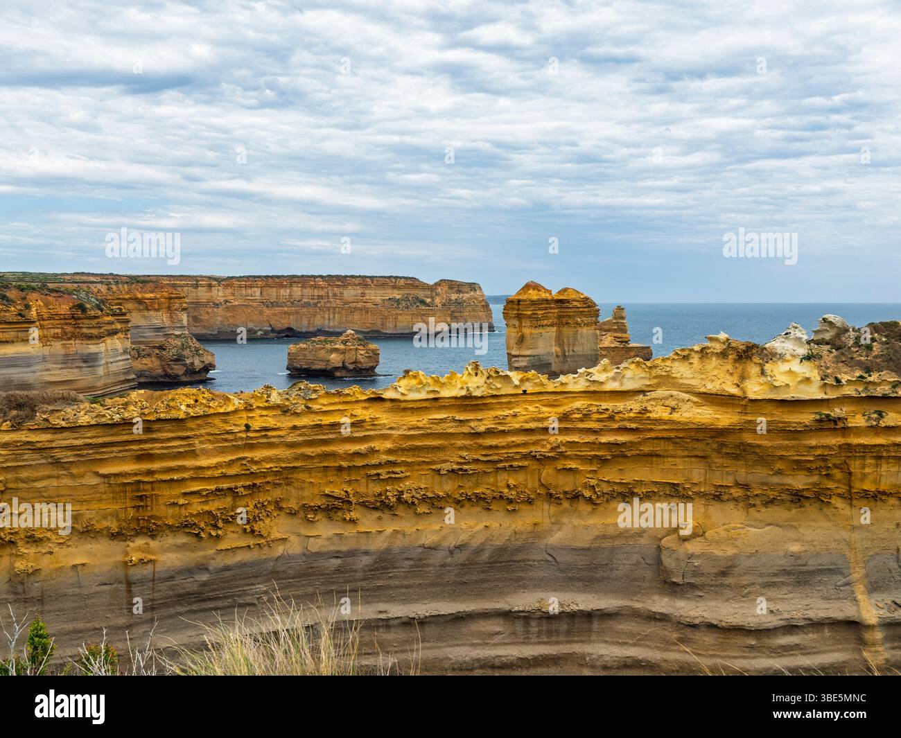 Splendide formazioni rocciose costiere sotto un cielo nuvoloso nei dodici Apostoli, Australia. Strati di roccia testurizzata creano un primo piano spettacolare, con il Foto Stock
