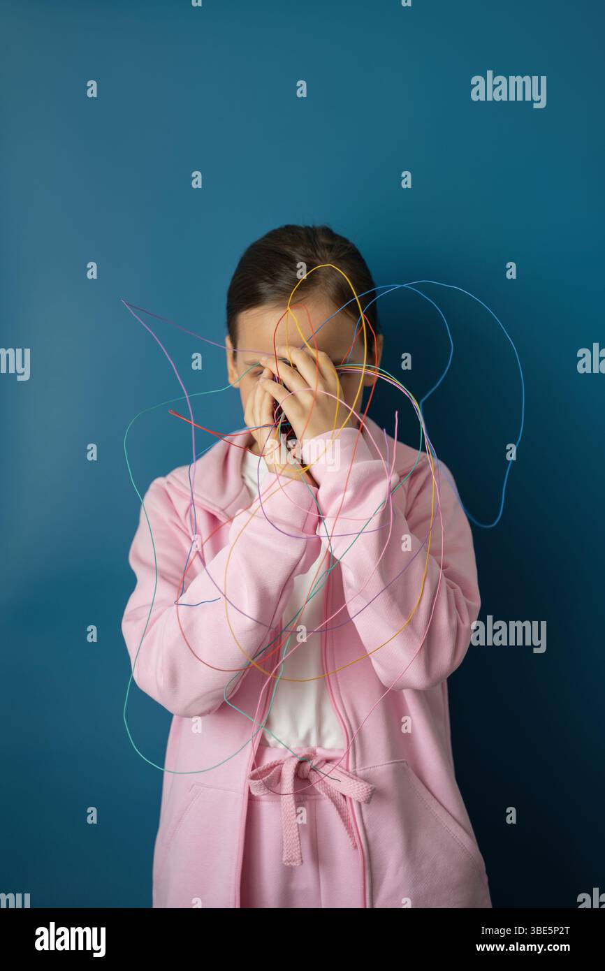 Un bambino con un abito rosa si erge su uno sfondo blu, aggrovigliato da fili colorati, a simboleggiare il complesso impatto di Internet e della tecnologia su Foto Stock