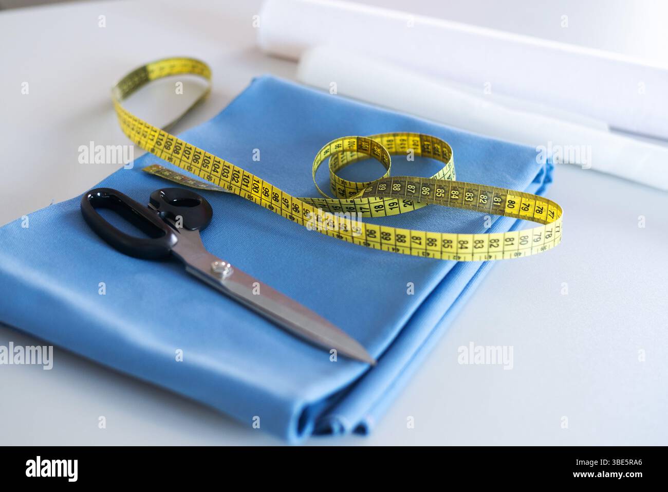 Un pezzo piegato di tessuto blu con un metro giallo e forbici da sarto poste sopra, che rappresentano attività di cucito, sartoria e sartoria Foto Stock